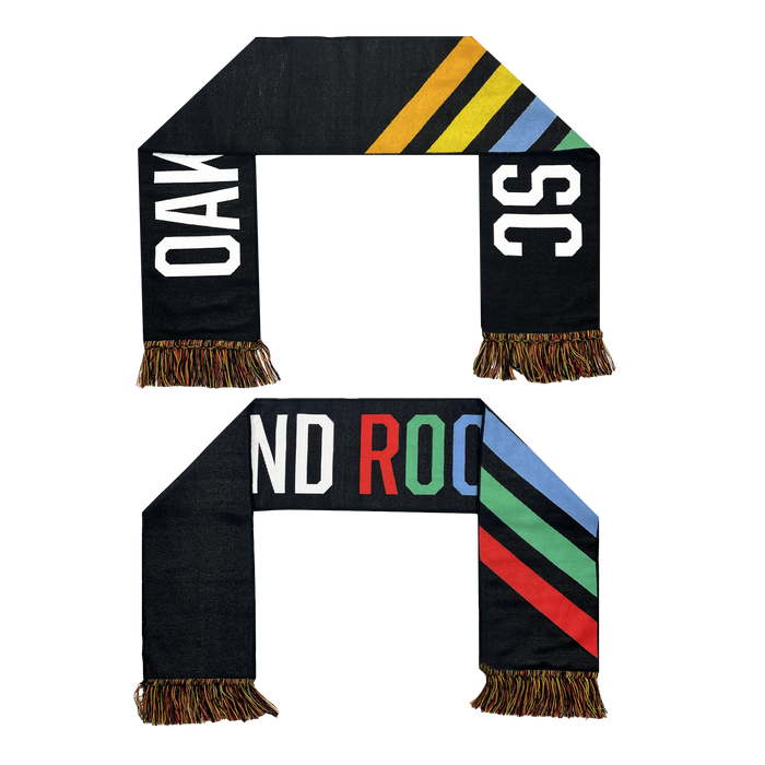 An Oakland Roots SC Alternative HD Woven Scarf featuring fringes at both ends. One side displays "OAK" in white letters, accompanied by diagonal stripes in yellow, green, blue, and red shades. The reverse side reads "LAND ROCK" in white, red, and blue letters with the same vibrant diagonal stripes—proudly supporting the social good mission of the Oakland Roots Sports Club.