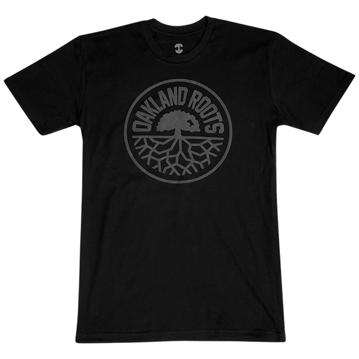 Introducing the Oakland Roots SC Blackout Logo Tee, a black T-shirt proudly featuring a circular emblem at its center. The text "OAKLAND ROOTS" is elegantly arched along the outer edge of the circle, enclosing an intricate illustration of a tree with expansive roots. This design symbolizes both Oaklandish pride and unwavering support for your favorite sports club. The dark-shaded design elements create a subtle yet striking contrast against the black fabric, making it a must-have for any fan.