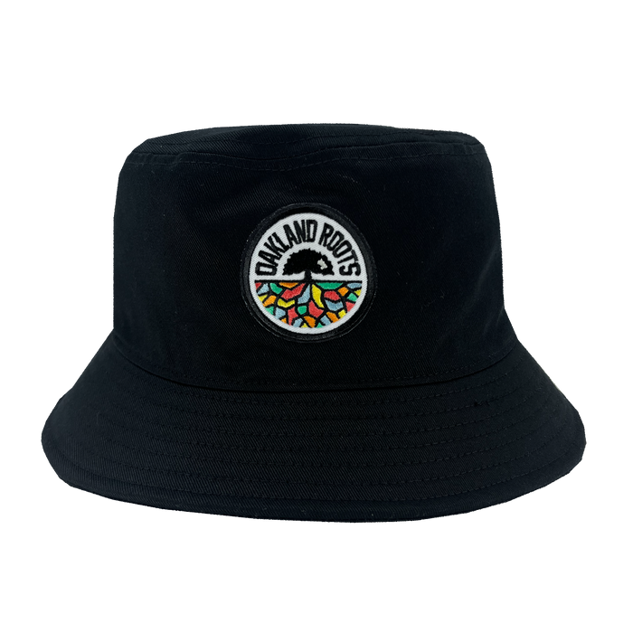 The Oakland Roots SC Bucket Hat by Oakland Roots SC is a black hat featuring a round embroidered patch on the front with "OAKLAND ROOTS" written on it. The patch also showcases a stylized tree with multicolored roots spreading out in a semi-circular pattern, including red, green, yellow, and blue, symbolizing the vibrant spirit of the sports club.