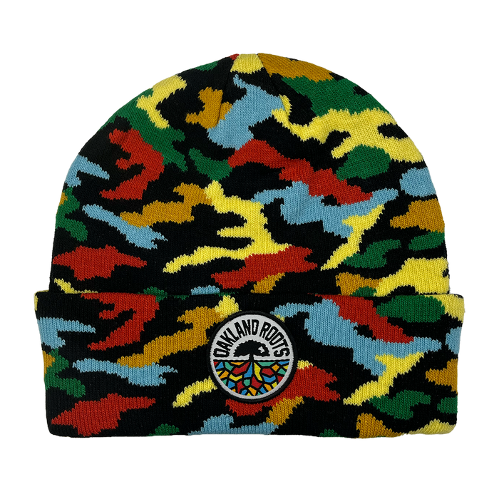 The Oakland Roots SC Camo Beanie is a knitted hat with a colorful camouflage pattern, a folded brim, and an Oakland Roots patch featuring the brand name and multicolored tree logo at the center.