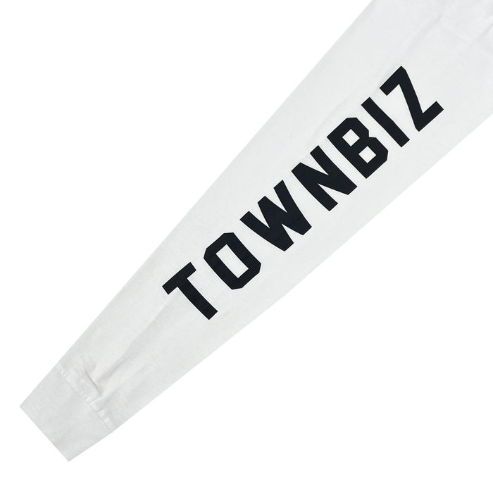 Close-up of the sleeve of an Oakland Roots SC Classic 2.0 LS Tee, showcasing the text "TOWNBIZ" in bold black capital letters printed vertically along the length of the smooth white fabric. The clearly legible text runs along the forearm section, celebrating Oakland Roots Sports Club’s vibrant sports culture.