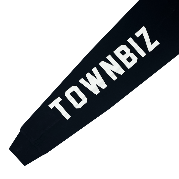 Close-up of a black sleeve featuring bold, white, uppercase text that reads "TOWNBIZ." The sleeve appears to be part of the Oakland Roots SC Classic 2.0 LS Tee by Oakland Roots SC, and the text runs along the length of the sleeve. The background is plain white.