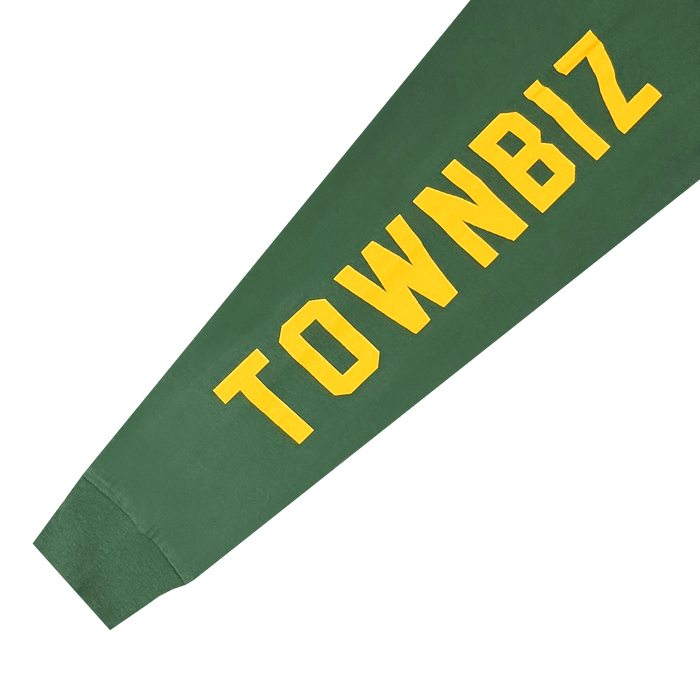 The Oakland Roots SC Classic 2.0 LS Tee features "TOWNBIZ" in bold yellow block letters diagonally on the green sleeve—a tribute to Oakland Roots SC and its commitment to community-driven social good.