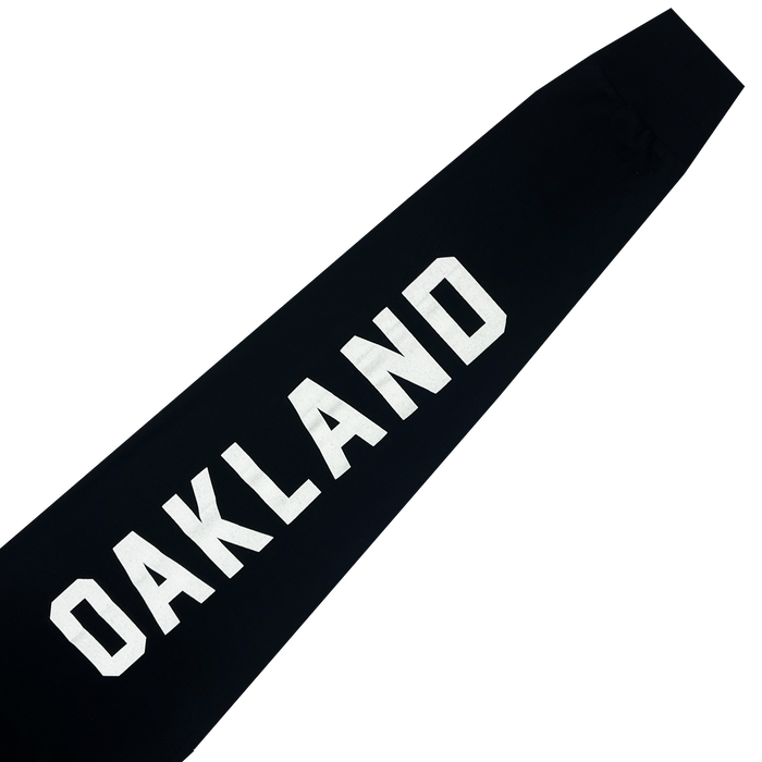 The Oakland Roots SC Classic 2.0 LS Tee is a black long-sleeve t-shirt featuring the word "OAKLAND" in large, bold, white letters diagonally positioned across the front from the bottom left to the top right. Set against a dark background, this soft, cotton-like garment is ideal for fans of the Oakland Roots sports club.