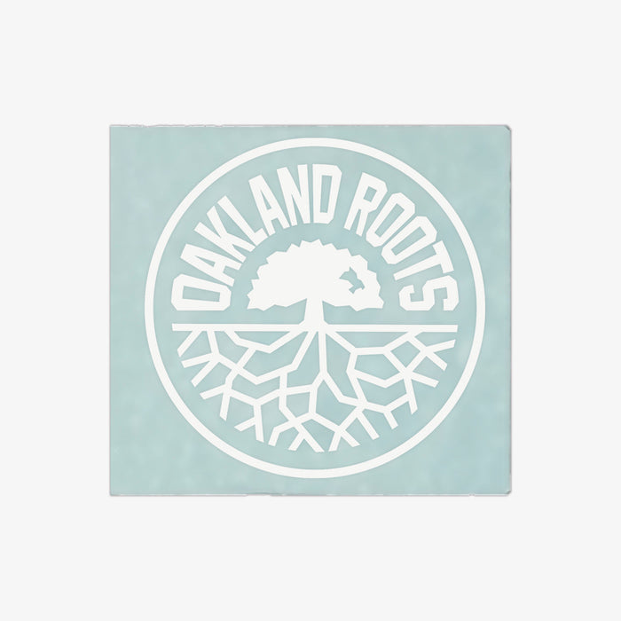 The Oakland Roots SC Decal - 6" features a pale blue-green background with a white circular logo. "OAKLAND ROOTS" is written in all caps along the top edge inside the circle, while a simplified tree with visible roots is centered within it, symbolizing Oakland Roots Sports Club's deep connection with its community. This decal is perfect for adorning your window!