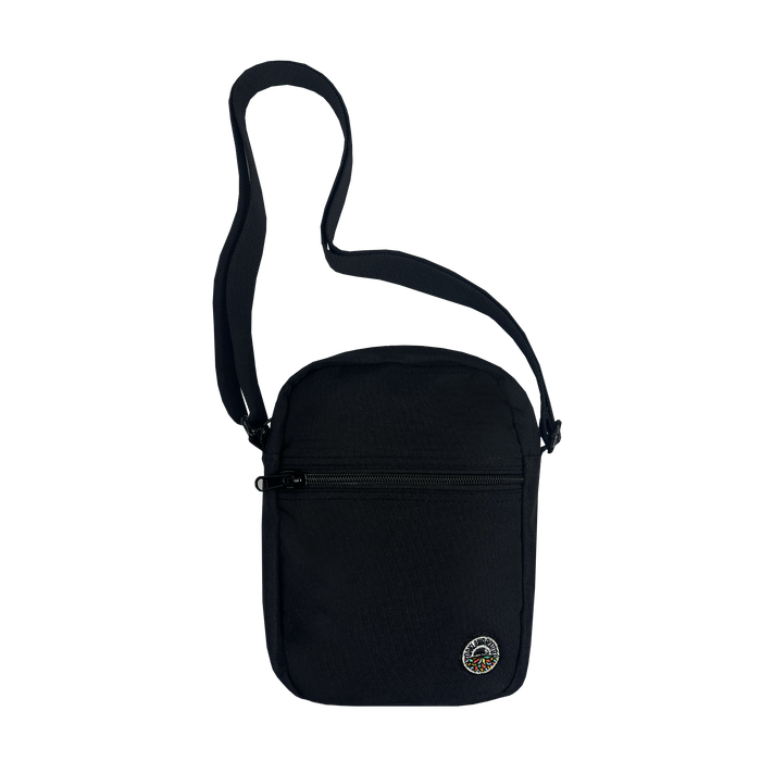 The Oakland Roots SC Flight Bag, a small black shoulder bag from Oakland Roots SC, is showcased. It includes a single adjustable strap and features a zippered front compartment along with a circular patch at the bottom right corner, adorned with colorful designs inspired by the Oakland Roots Sports Club. Made from durable fabric, this bag is ideal for everyday use.