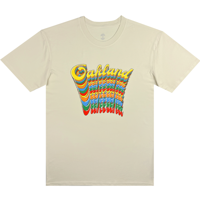 Introducing the Oakland Roots SC Funk Tee by Other: this beige t-shirt showcases “Oakland” in bold, yellow, 1970s-inspired wavy lettering above stacked rainbow waves on the front center, creating a colorful retro-psychedelic look—ideal for fans of the Oakland Roots Sports Club.