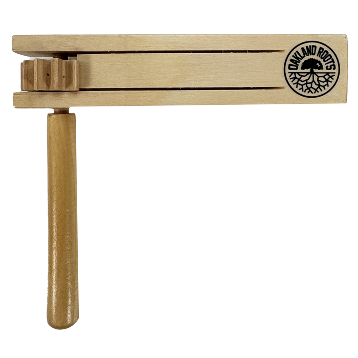 The Oakland Roots SC Matraca is a wooden noisemaker featuring the Oakland Roots SC logo with bold text and a striking tree graphic. It includes a handle, rotating mechanism, two horizontal slats, and gear-like parts for sound, embodying Oakland's spirit.