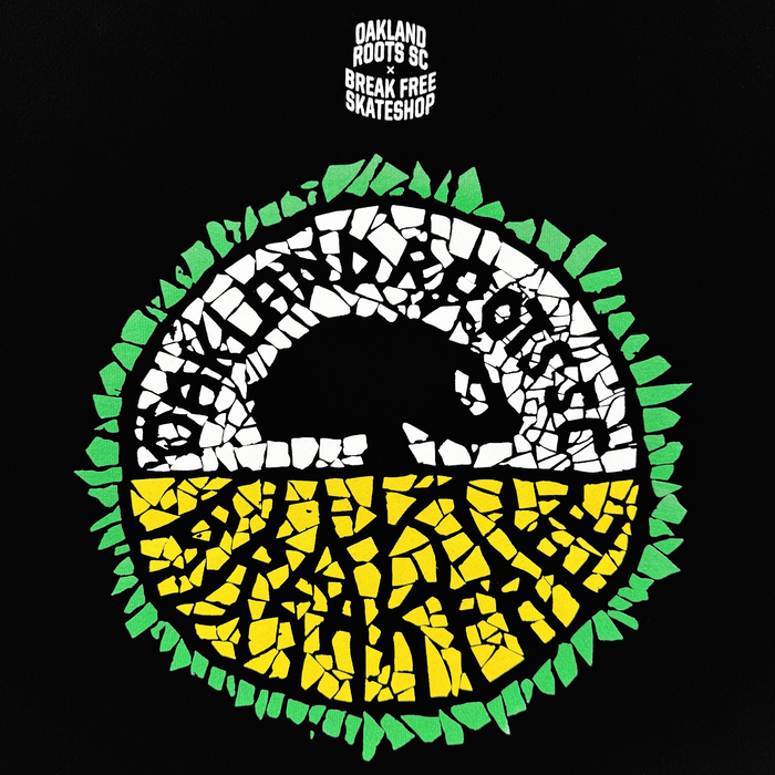 The Oakland Roots SC X Break Free Tee features a circular mosaic logo with “OAKLAND ROOTS” in white around a black bear silhouette. The top is white, the bottom yellow with green roots. "OAKLAND ROOTS SC x BREAK FREE SKATESHOP" appears above in white on black.