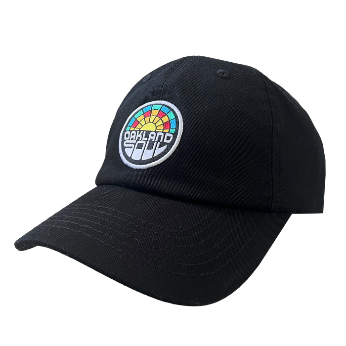 The Oakland Soul Dad Hat is a black baseball cap adorned with a multicolored circular patch on the front. The patch showcases the text "OAKLAND" in white and "SOUL" in black, set against a rainbow design featuring red, orange, yellow, green, and blue segments. This cap celebrates the Oakland Soul women's soccer team in the USL W-League.