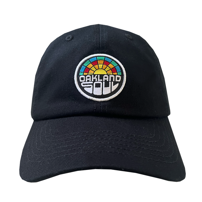 The Oakland Soul Dad Hat is a black baseball cap featuring a circular, multicolored patch centered on the front. The patch showcases a stylized sunset design in shades of red, orange, yellow, green, and teal with the text "OAKLAND SOUL" in bold white letters beneath it—a perfect tribute to your favorite women's soccer team in the USL W-League.