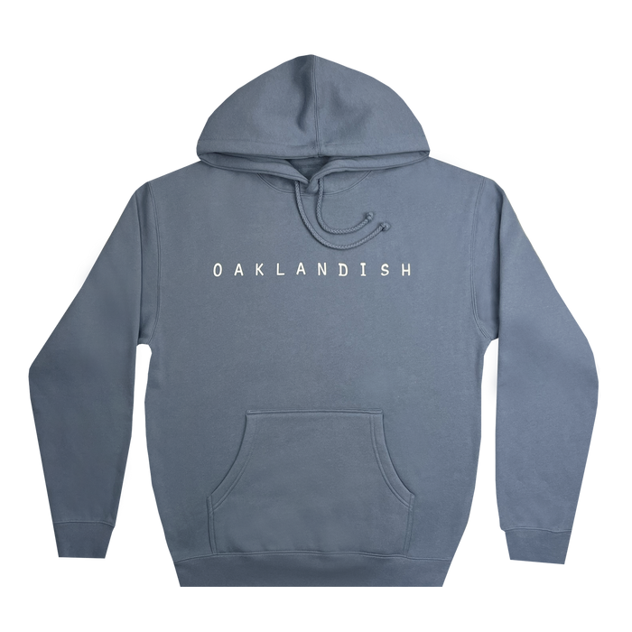 The Oaklandish Classic Hoodie by Oaklandish features a storm blue pullover design with a front pocket and drawstring hood. The chest displays "OAKLANDISH" in bold, white uppercase letters to celebrate Oakland pride. The hoodie is completed with ribbed cuffs and hem, offering a simple and casual aesthetic.