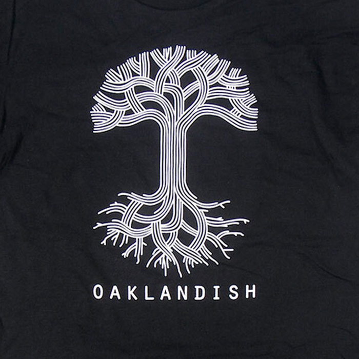 Close-up of large white Oaklandish tree logo and wordmark on the front chest of a black t-shirt.