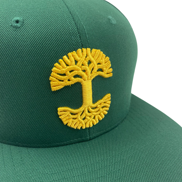 The Oaklandish Classic Snapback by Oaklandish is a green baseball cap with a yellow embroidered design on the front, resembling a tree with a stylized trunk and branches forming circular patterns at the top and bottom, reminiscent of the Oaklandish logo. This snapback cap features a flat bill with visible stitching along the seams.