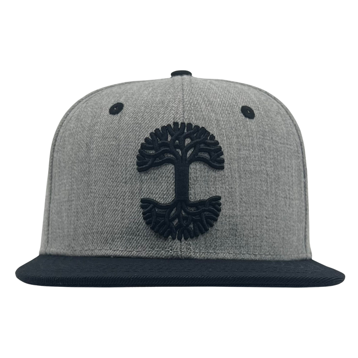 The Oaklandish Classic Snapback by Oaklandish features a flat black brim and a black embroidered tree logo on the front. The hat includes two small black air vents on either side of the logo and a round button on top, all set against a plain white background.