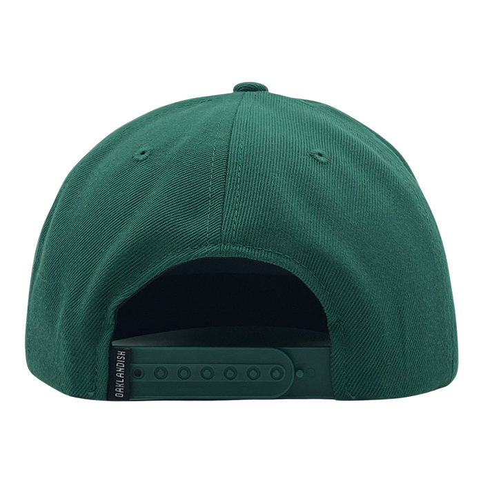 The Oaklandish Classic Snapback, a green baseball cap viewed from the back, showcases its stylish design with an adjustable snapback closure offering multiple size settings. The Oaklandish logo is printed in white on a small black tag located on the left side of the snap. The fabric of the cap features a slightly textured appearance.