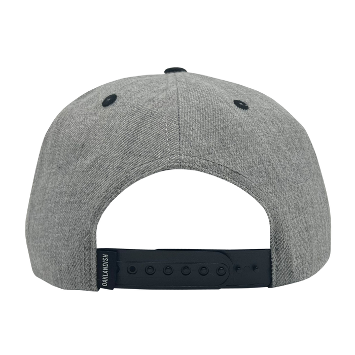 A gray Oaklandish Classic Snapback baseball cap is shown from the back. This headwear features a black adjustable snapback strap and two black ventilation eyelets on either side. A small black tag with white text is attached to the left side of the snapback strap.