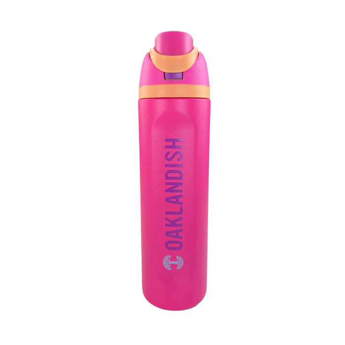 The Oaklandish Colorful Bottle features a bright pink body, orange accents, and a flip-top lid. "OAKLANDISH" is printed vertically in bold silver letters on the side, with a small circular logo below it. Set against a plain white background.