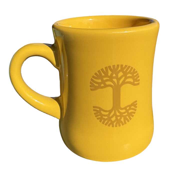 This Oaklandish Diner Mug, a striking piece from the renowned brand Oaklandish, showcases a smooth, curvy design with a left-sided handle. The yellow ceramic mug is beautifully adorned with a darker yellow stylized tree of life symbol, where the branches and roots reflect each other gracefully.