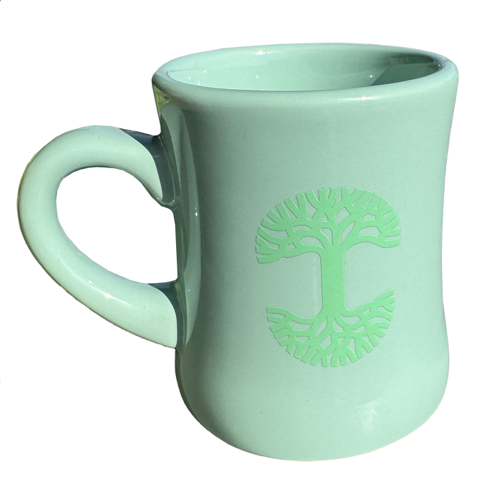 The Oaklandish Diner Mug by Oaklandish is a light green ceramic mug that boasts a stylized tree design embossed on one side. The symmetrical branches and roots of the tree form a circle, adding charm to the drinkware. Its curvy, slightly tapered shape and large handle stand out against a plain white background.