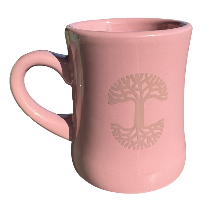 The Oaklandish Diner Mug, crafted by the brand Oaklandish, is a chic piece of ceramic drinkware featuring a pink color with a flared rim and a left-curved handle. Its embossed design highlights a stylized tree with symmetrical branches and roots at the center, while its glossy finish elegantly reflects light.
