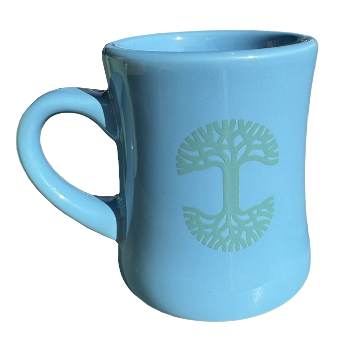 The Oaklandish Diner Mug is a light blue ceramic piece with a wide base and a narrow top, making it ideal for any drinkware collection. It features a green geometric tree design on one side, while the handle takes on a simple half-heart shape, set beautifully against a plain white background.