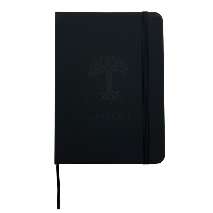 The "Oaklandish Emblem Journal" by Oaklandish is on display. This black notebook features a sleek PVC cover and an elastic band for closure. The front cover is embossed with the intricate Oaklandish tree logo above the word "OAKLANDISH" in all capital letters. The notebook also features rounded corners and a minimalist design.