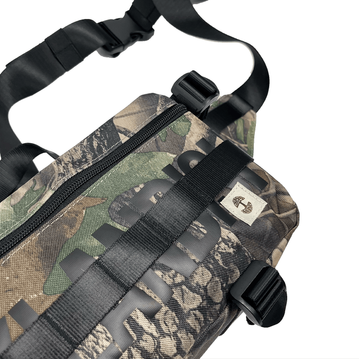 Top side view of a camo pattern cross-body bag with front zipper and large black Oakladish wordmark and Oaklandish tree logo patch.