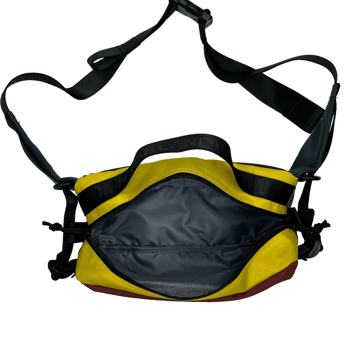 The Oaklandish Hip Bag by Oaklandish is a yellow and black shoulder bag featuring an open main compartment that reveals a spacious, grey-lined interior. This versatile bag comes with adjustable black straps and additional side clasps for support, while the bottom is maroon. Its unisex appeal and premium details make it stand out against a plain white background.