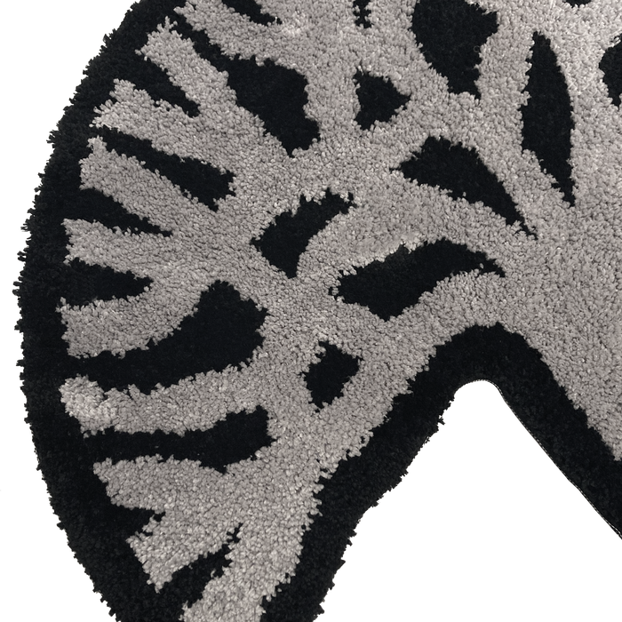 A close-up view of the Oaklandish Logo Rug by Oaklandish, showcasing a curved design with an abstract geometric pattern. The motif features light gray and black sections, creating a dynamic, asymmetrical appearance. The texture appears soft and plush, adding depth and visual interest to the Oaklandish-inspired design.