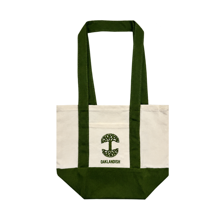 The Oaklandish Mini Grocery Tote by Oaklandish features green straps and a bottom, with an embroidered green tree logo above the word “OAKLANDISH” in green on a cream-colored background at the center. This mini tote is a simple yet sturdy accessory, ideal for carrying everyday items.