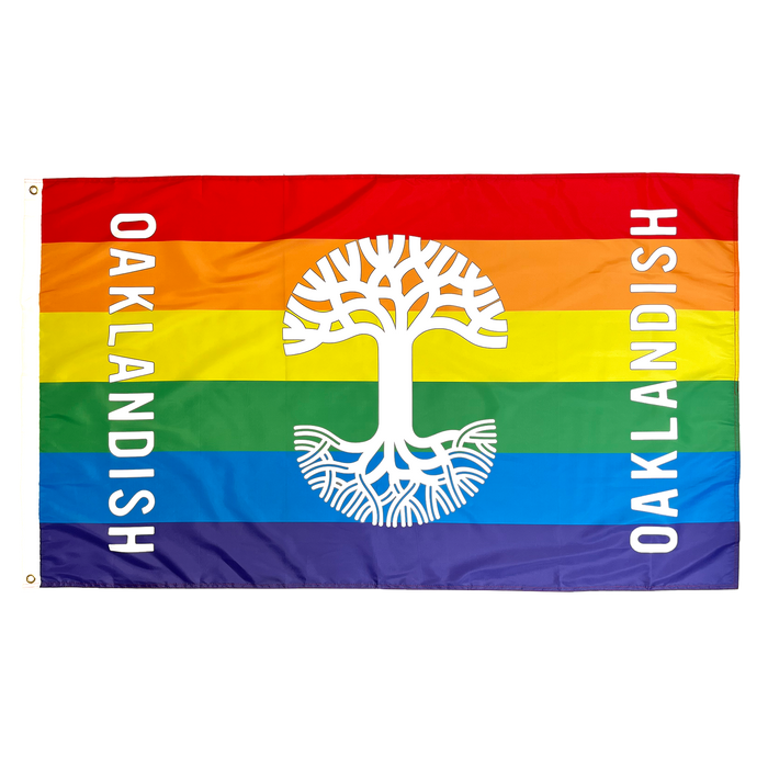 The Oaklandish Pride Logo Flag, crafted by Oaklandish, features a rectangular design with horizontal stripes in the rainbow colors: red, orange, yellow, green, blue, and purple. At the center is a white stylized tree. "OAKLANDISH" is written vertically in white on both sides of this knit polyester flag—a perfect accessory for any space.