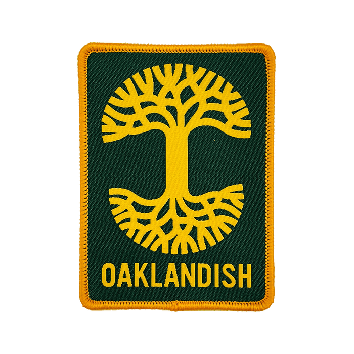 The Oaklandish Rectangle Patch by Oaklandish is a rectangular patch featuring a dark green background with yellow stitching around the edges. The embroidered iron-on patch showcases a stylized yellow tree with symmetrical roots and branches extending from a central trunk. Below the tree, "OAKLANDISH" is written in yellow capital letters, representing Oakland.