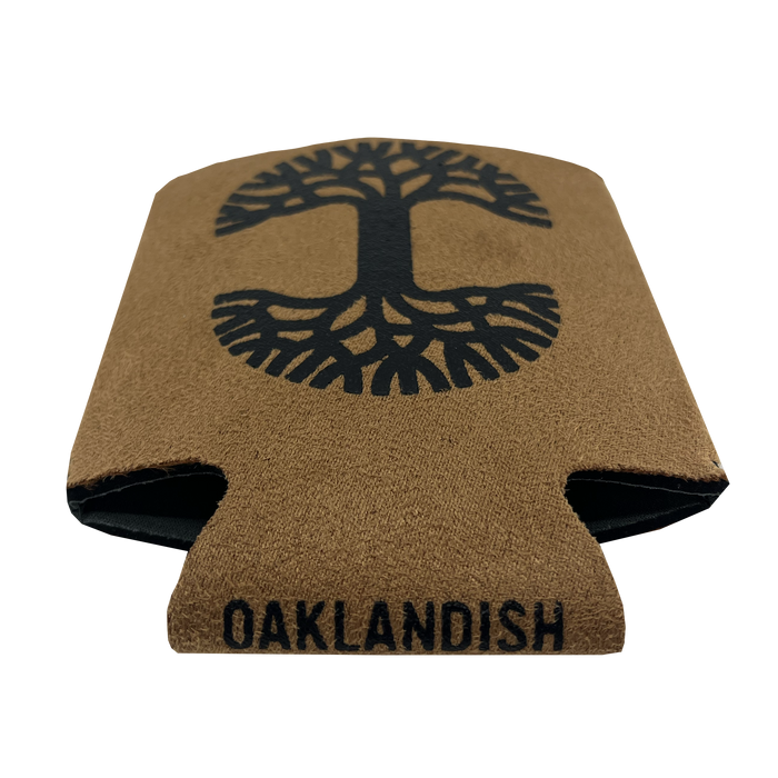 The Oaklandish Suede-ish Can Cooler features a brown exterior with a black abstract tree design on the front. "OAKLANDISH" is printed in black capital letters at the bottom. The collapsible cooler has a neoprene interior and folds flat for convenient storage.