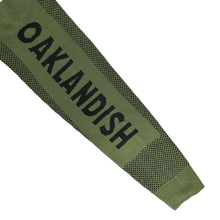 The Oaklandish Terrace Sweater features a long olive-green knit in men's sizing, with black mesh accents and bold vertical “OAKLANDISH” text. This army-inspired design by Oaklandish pops against a white background.