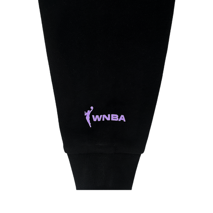 Close-up of a black Odin Hoodie sleeve cuff by GSV, showing the lavender WNBA logo and embroidered text near the wrist. Officially licensed unisex apparel with a stylized figure and “WNBA.” Plain light gray background.