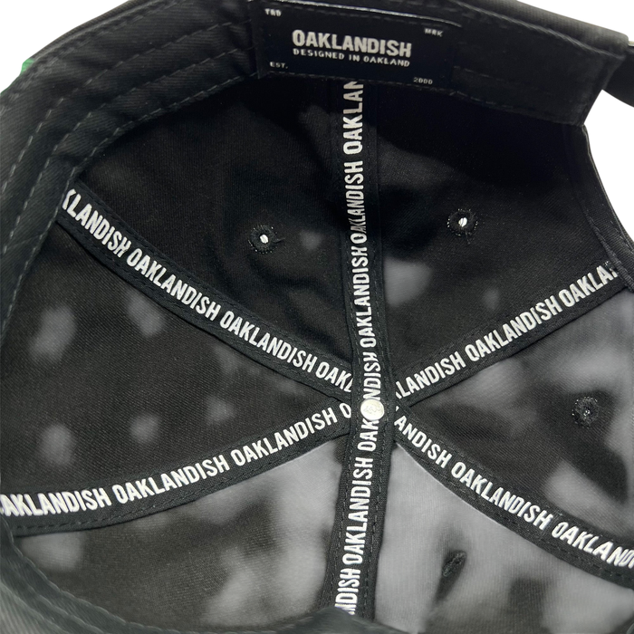 The interior view of the Official Micro Logo Dad Hat in black showcases the brand "Oaklandish" printed repeatedly along the inner seams. A label on the inside reads "Oaklandish Designed in Oakland Est. 2000." The cap features an embroidered "O" and multiple triangular sections converging at the top button.