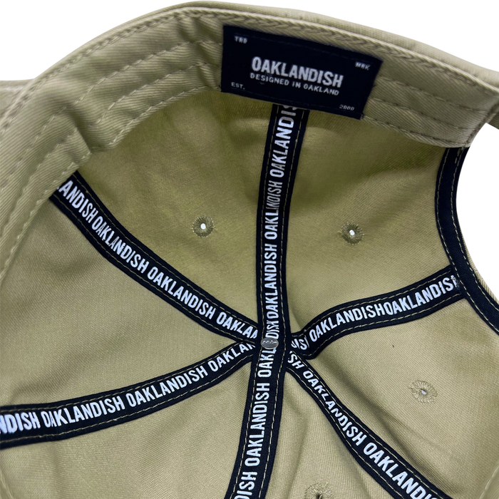 The image reveals the interior of an Oaklandish Official Micro Logo Dad Hat. The black fabric bands, imprinted with "Oaklandish" in white, fan out from the center of the crown. Inside, a tag reads, "Oaklandish, designed in Oakland, Est. 2000." The hat features an adjustable strap for a perfect fit.