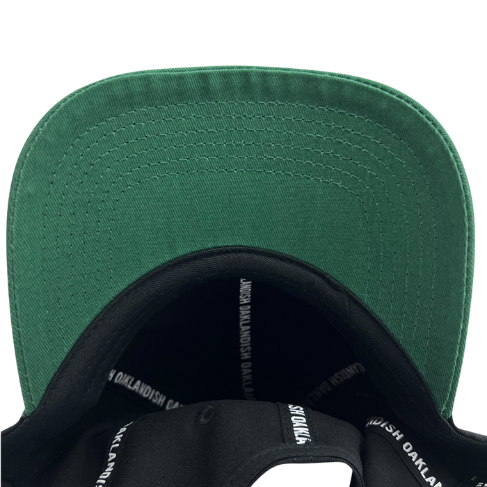 A close-up view of the underside of the Official Micro Logo Dad Hat's green brim. The inner band is black, adorned with "OAKLANDISH" repeatedly printed in white. From this bottom-up perspective, you can also notice an embroidered "O," adding a unique touch to the Oaklandish design.