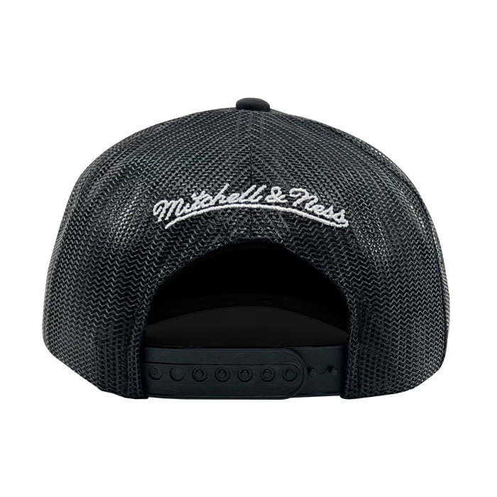 The image showcases the back of an Official O Trucker hat by Oaklandish, featuring "Mitchell & Ness" embroidered in white cursive lettering on the adjustable black mesh closure. The hat sports a curved opening for the head and snap buttons to ensure a perfect fit.