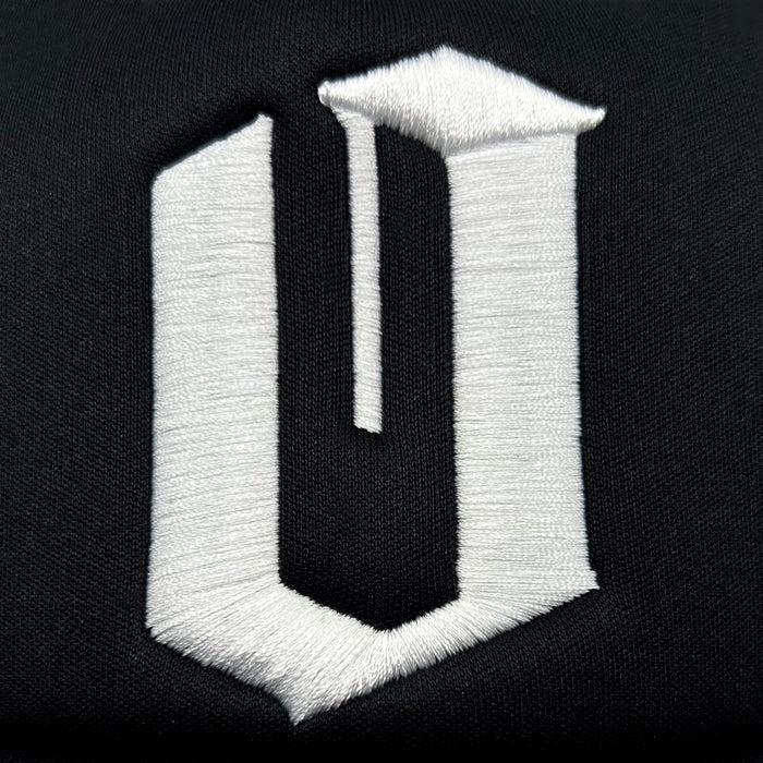 The image features a stylized, embroidered letter "U" in white thread on a black fabric background. It has a three-dimensional appearance with sharp, clean edges, similar to the bold and striking contrasts typical of Oaklandish's Official O Trucker hats.