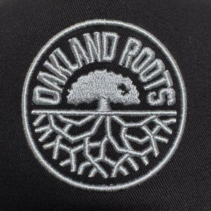 The ORSC 5 Panel Hat by Oakland Roots SC features a light gray embroidered tree with exposed roots inside a circle on black fabric, with "OAKLAND ROOTS" arched above—a standout piece of Oakland sports club merchandise.