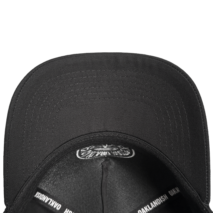 A top-down view of the black ORSC 5 Panel Hat by Oakland Roots SC, showing the underside of its brim and inside panels with "OAKLANDISH" repeatedly printed in white—a standout piece for Oakland Roots SC fans.