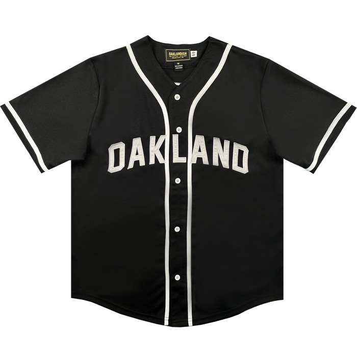 Here’s a rewritten sentence using your product data: The ORSC Button Up Jersey by Oakland Roots SC is a black short-sleeve baseball jersey with white trim on the sleeves and collar, featuring "OAKLAND" in bold white letters across the chest. Inspired by the Oakland Roots Sports Club, it includes white buttons down the front and a black tag at the inside collar.