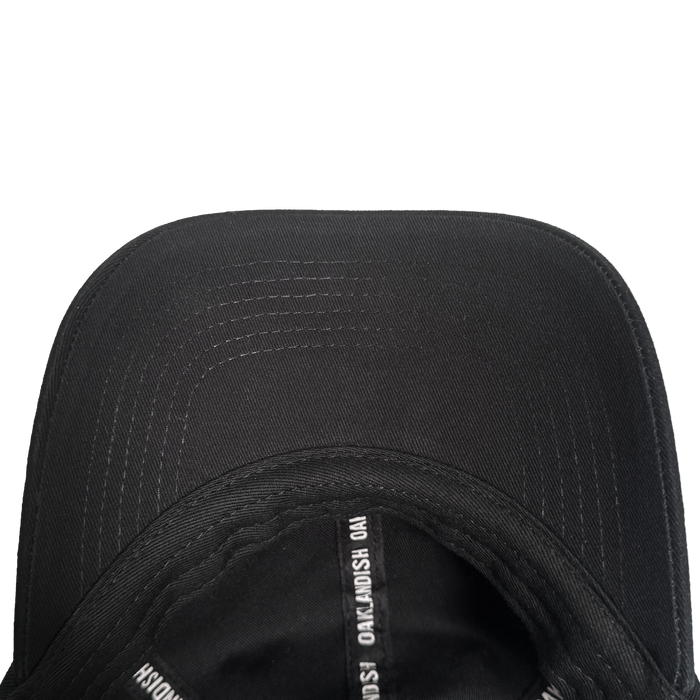 A close-up of a black Oakland Roots SC ORSC Dad Hat shows its curved brim with visible stitching arcs. The inner seam tape repeats white "NOAK MOSH" text on black. The background is plain white.