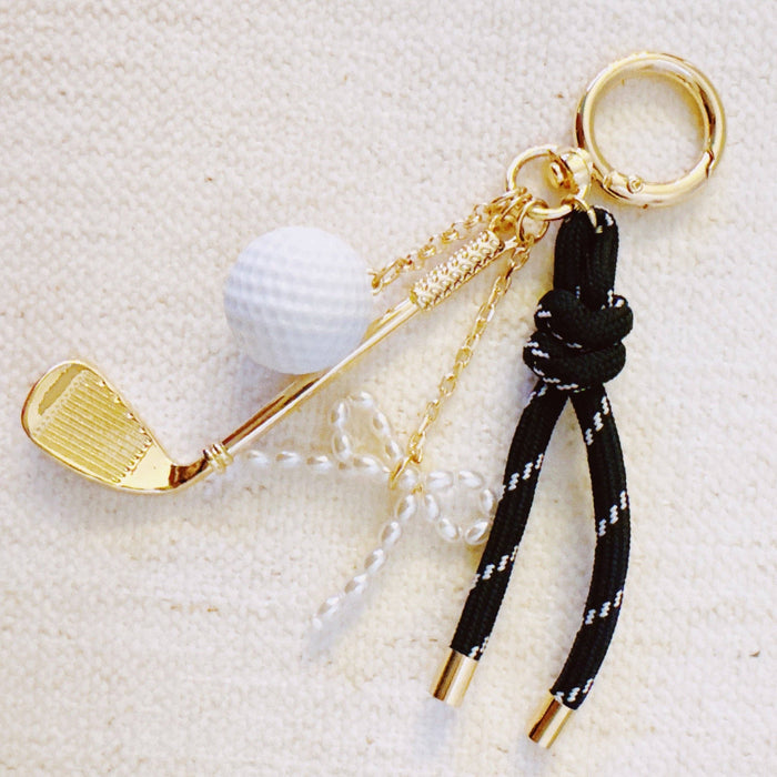 Ellison+Young Par Tee golf bag charm with gold and forest green accents, featuring golf club and ball charms.