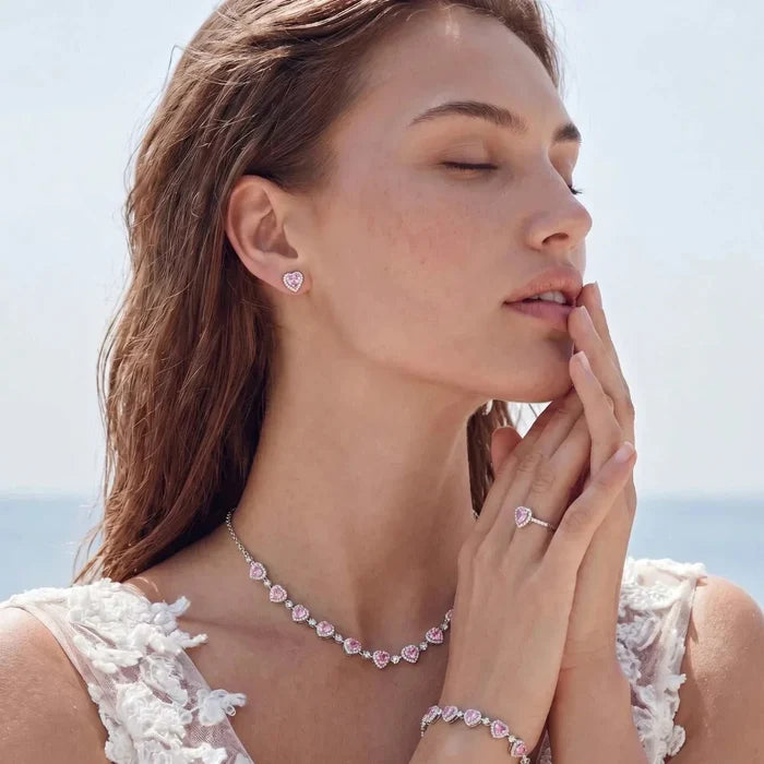 Pink Heart Zirconia jewelry set in silver-tone metal, worn as a heart pendant necklace, matching earrings, ring and bracelet