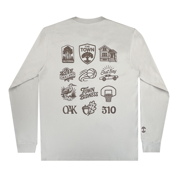 The Pirate Black-Letter LS Tee by Other is a light gray long-sleeve shirt featuring black illustrations on the back—trees, houses, a basketball, and text like "California," "The Town," "East Bay," "Oakland," "Town Bidness," "OAK," and "510." Part of the Warriors x Oaklandish Town Collection, it celebrates local pride with a small logo detail on the left sleeve cuff.