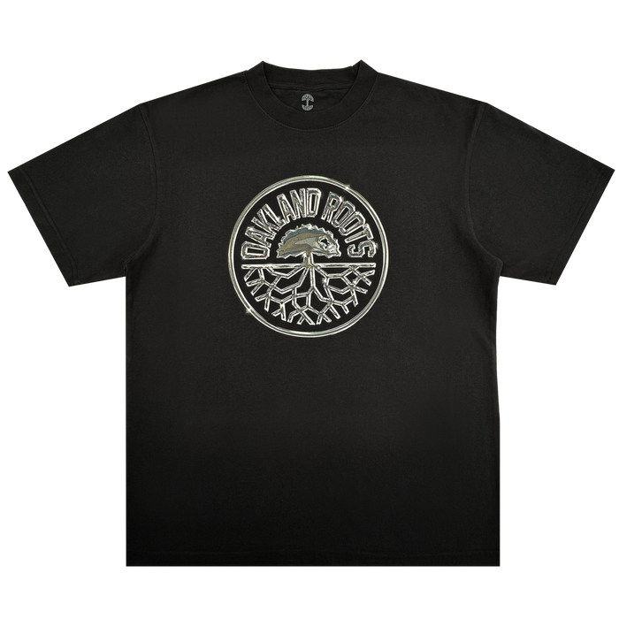 The Platinum Crest Tee by Oakland Roots SC is a black classic-fit t-shirt with a bold circular "OAKLAND ROOTS" logo in white and gray, featuring the iconic tree crest—perfect for any Oakland Roots SC fan.