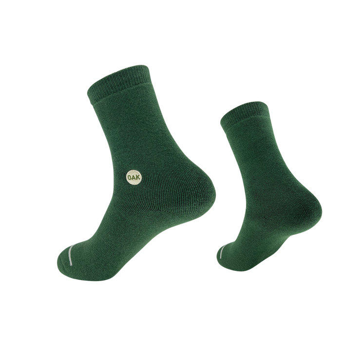 A pair of green Plush Oak Socks from Oaklandish is displayed against a plain white background. Crafted from soft cotton, these socks feature a ribbed cuff and a small circular "OAK" logo on the side. Artfully arranged, one sock presents a side view while the other is slightly elevated, promising happy feet.